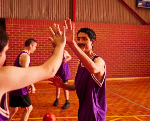 Basketball players dressed in purple jerseys high five after scoring a goal. They are located in an indoor basketball court.